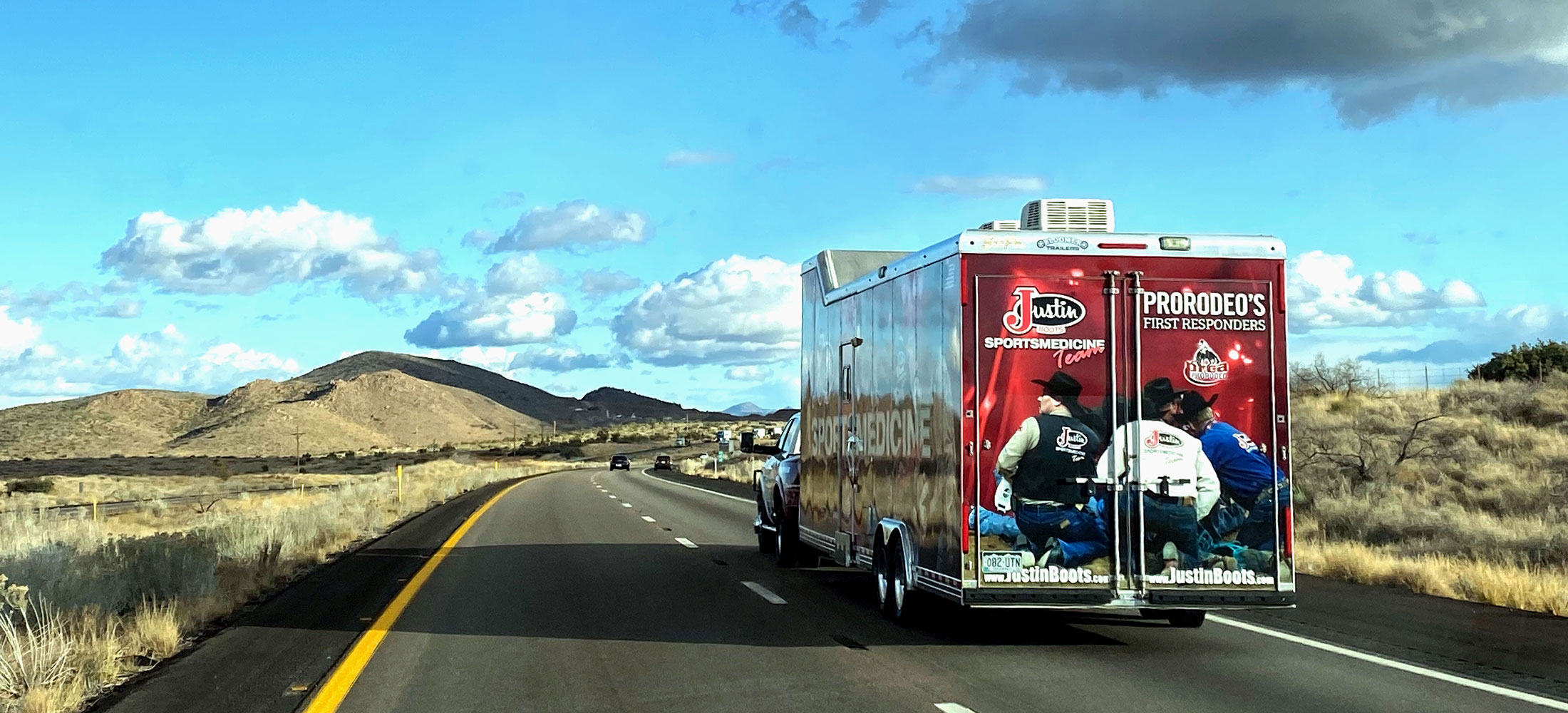 A red, black and white trailer driving away from the camera into the blue skies on the road.